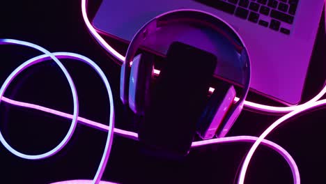 composition of laptop, headphones and smartphone with pink neon lights on black background