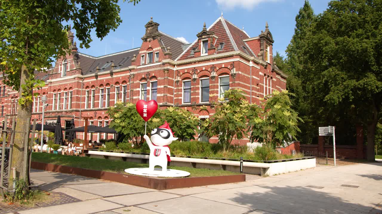 Camera slowly pans left past cartoon statue with balloons in bright city park setting