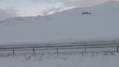 Fpv-shot,-girl-walking-on-winter-road-by-ocean-shore,-house-in-background