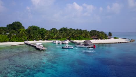 island in maldives - tropical paradise of palm trees and white sand with boats, wooden footbridge, and beach villa on the aqua blue sea water - a perfect tourist destination - wide shot