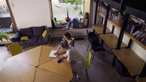 Two-adult-female-students-discussing-new-project-in-library,-high-angle-view