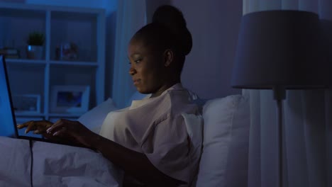 African-Woman-with-Laptop-in-Bed-at-Home-at-Night.technology,-internet,-communication-and-people-concept-young-african-american-woman-with-laptop-computer-lying-in-bed-at-home-at-night