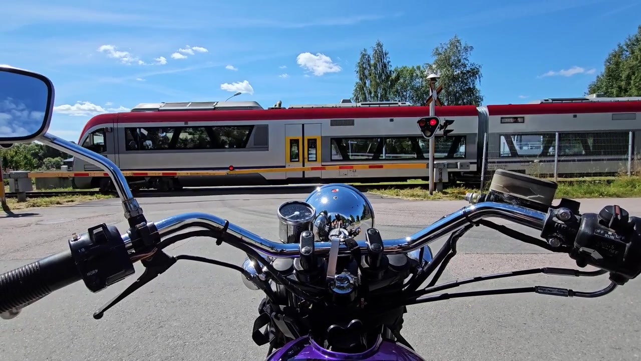 Motociclista in attesa mentre un treno passa, estate in Svezia