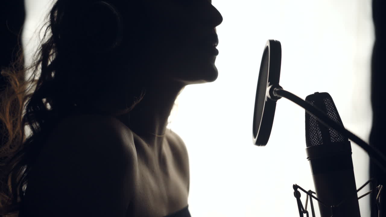 Young woman with bare shoulders recording a song in a professional studio. Female moving her shoulders and singing. Black and White.