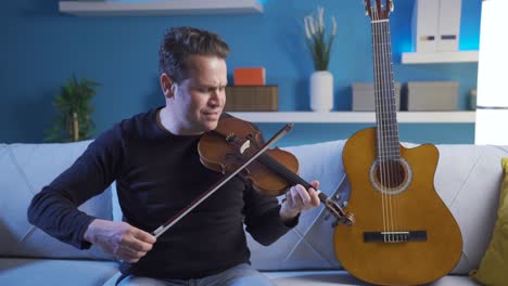 male musician sitting on the sofa at home playing the violin and composing a new song, playing a song he knows.