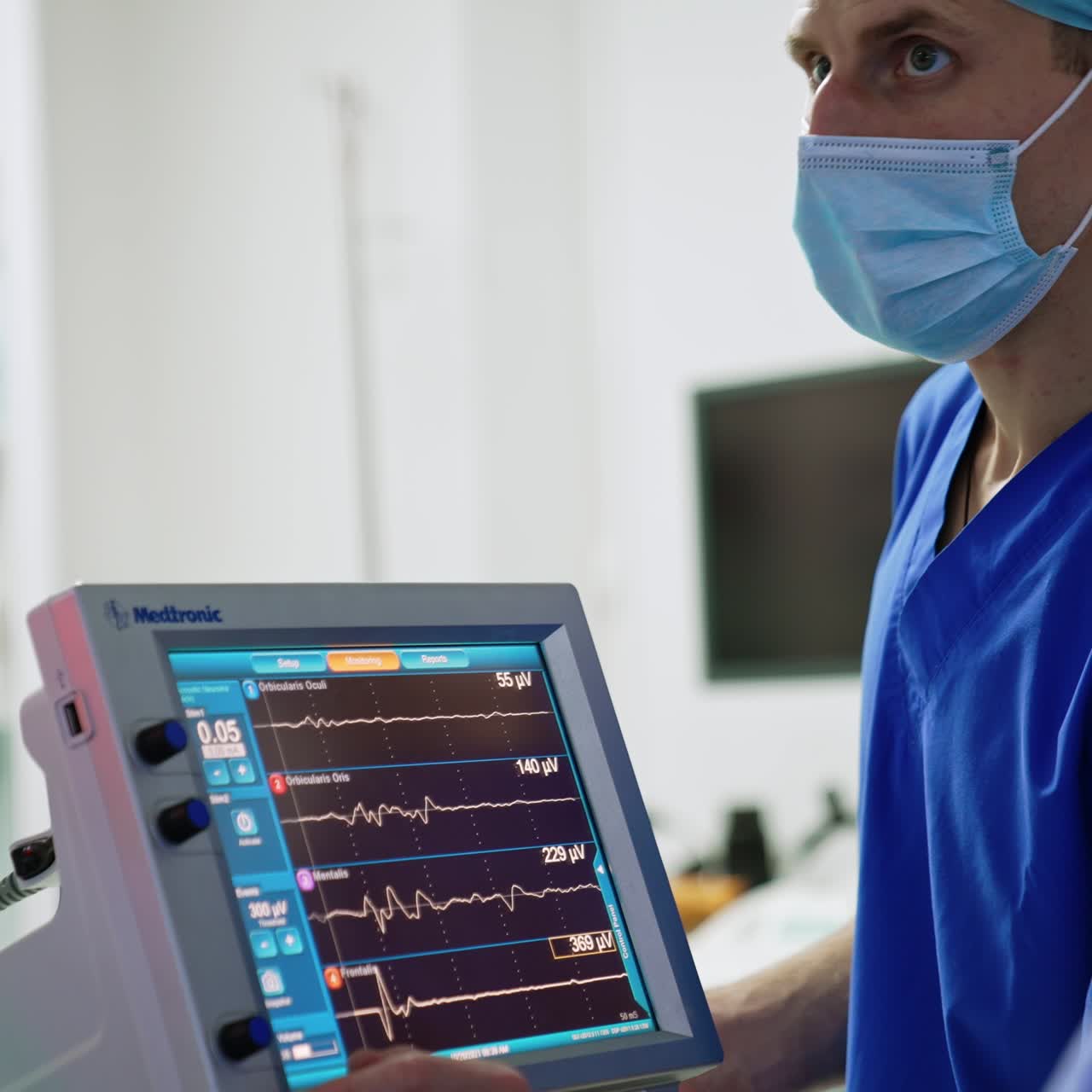 Médico caucásico con mascarilla y gorro de pie cerca de la pantalla de un ventilador pulmonar artificial. Retrato de un asistente trabajando en quirófano.