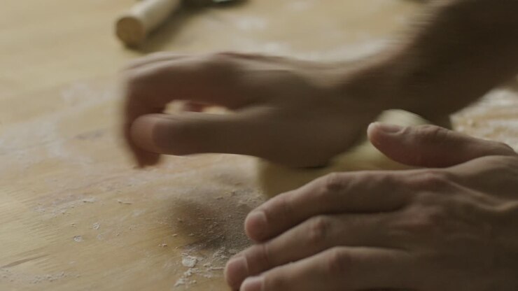 Hands of Man Kneading Dough on Floury Wooden Table