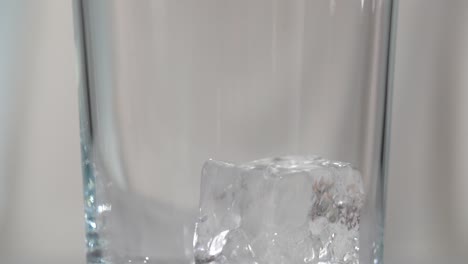 macro ice cubes being dropped into clear tall glass with white background slow motion 4k