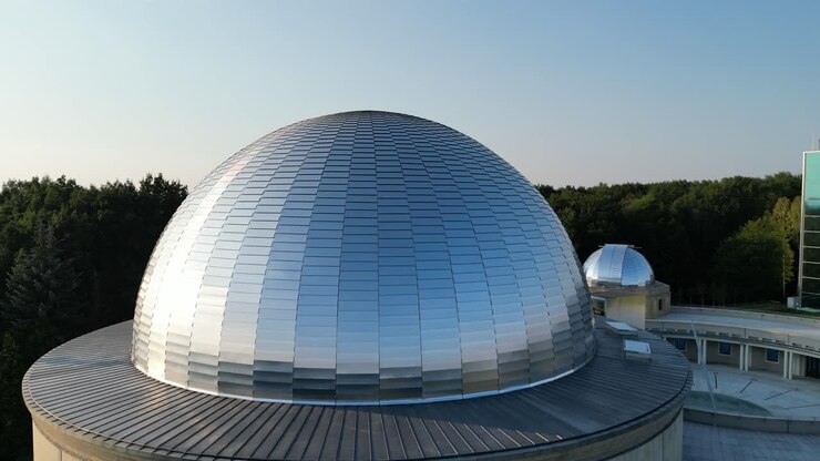 Observatorio astronómico durante un hermoso día de verano, rodeado de exuberante vegetación, césped y árboles bajo un cielo azul claro
