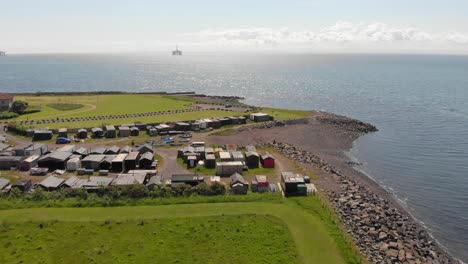cabañas de pesca de chabolas sobrevuelan con pequeños botes listos para ser arrastrados al mar con una plataforma petrolera en el fondo