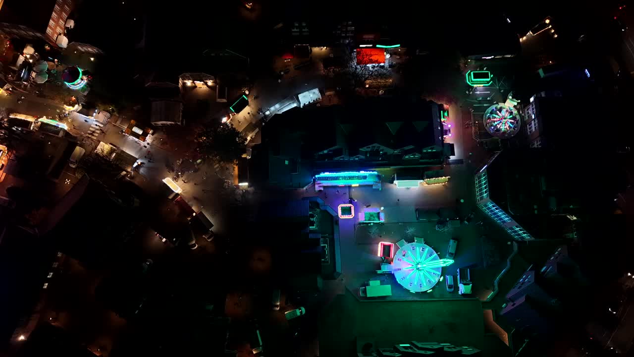 Vibrant nighttime aerial of an American festival with bright neon rides, food stands and crowds in USA. Lively fairground atmosphere from above in glowing colors. Aerial top down shot