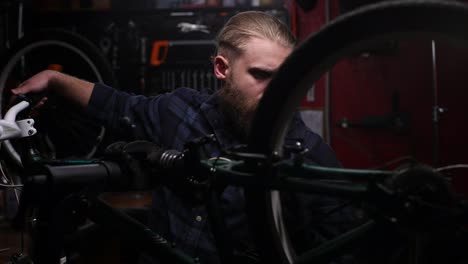 close-up of skilled bike repairman watching rear shifter of mountain bike, changing speeds using handlebar shift lever working in dark garage