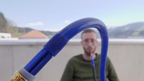 joven caucásico fumando narguile con una manguera azul al aire libre, cámara lenta