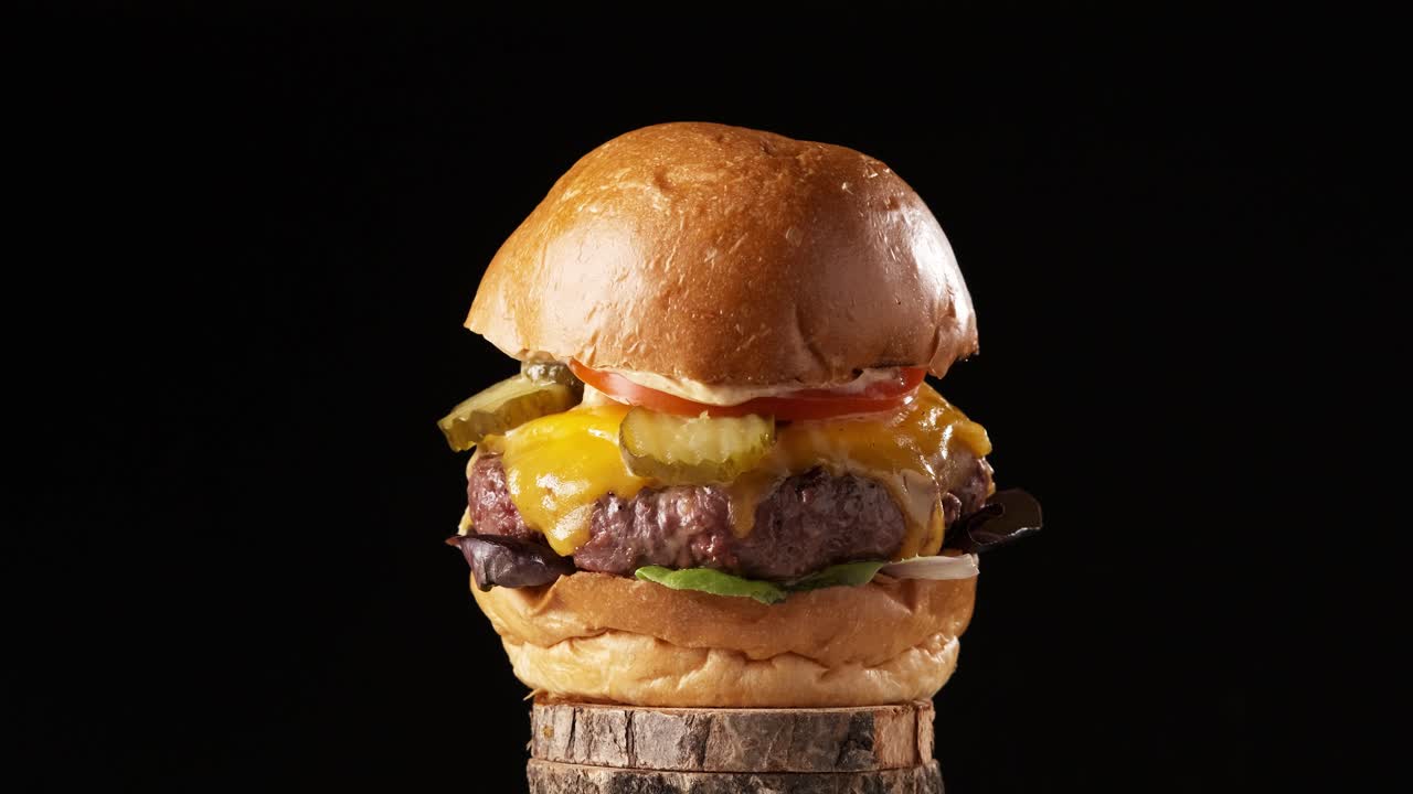 Juicy cooked beef burger with cheese rotating on black background. Looks real. Slow motion