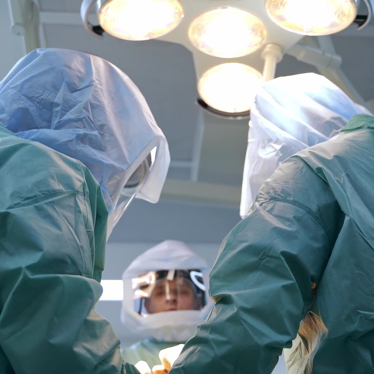 Team of surgeons in protective suits performing trauma operation. Low angle view. Lamps at the ceiling at backdrop