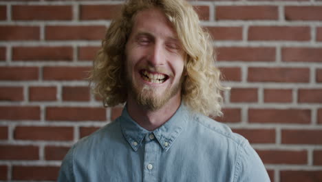 portrait happy young blonde man student laughing enjoying successful lifestyle cheerful bearded hipster guy looking at camera brick wall background