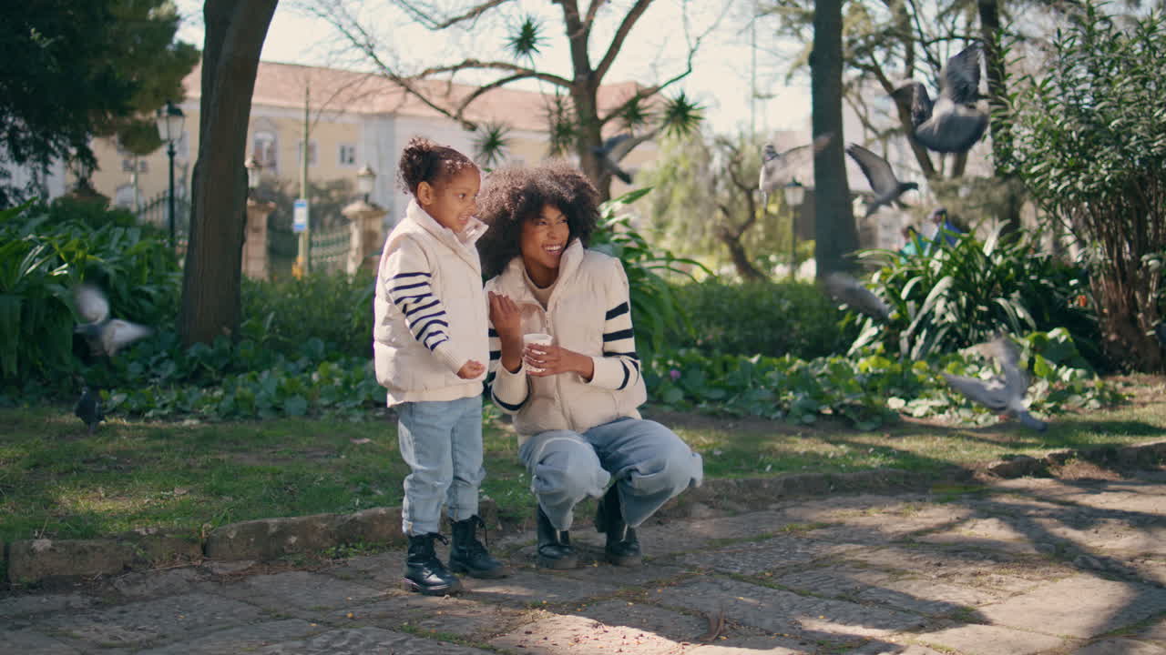 공원 위에서 날아다니는 비둘기를 먹이는 어머니 소녀. 귀여운 아이가 씨을 던집니다.