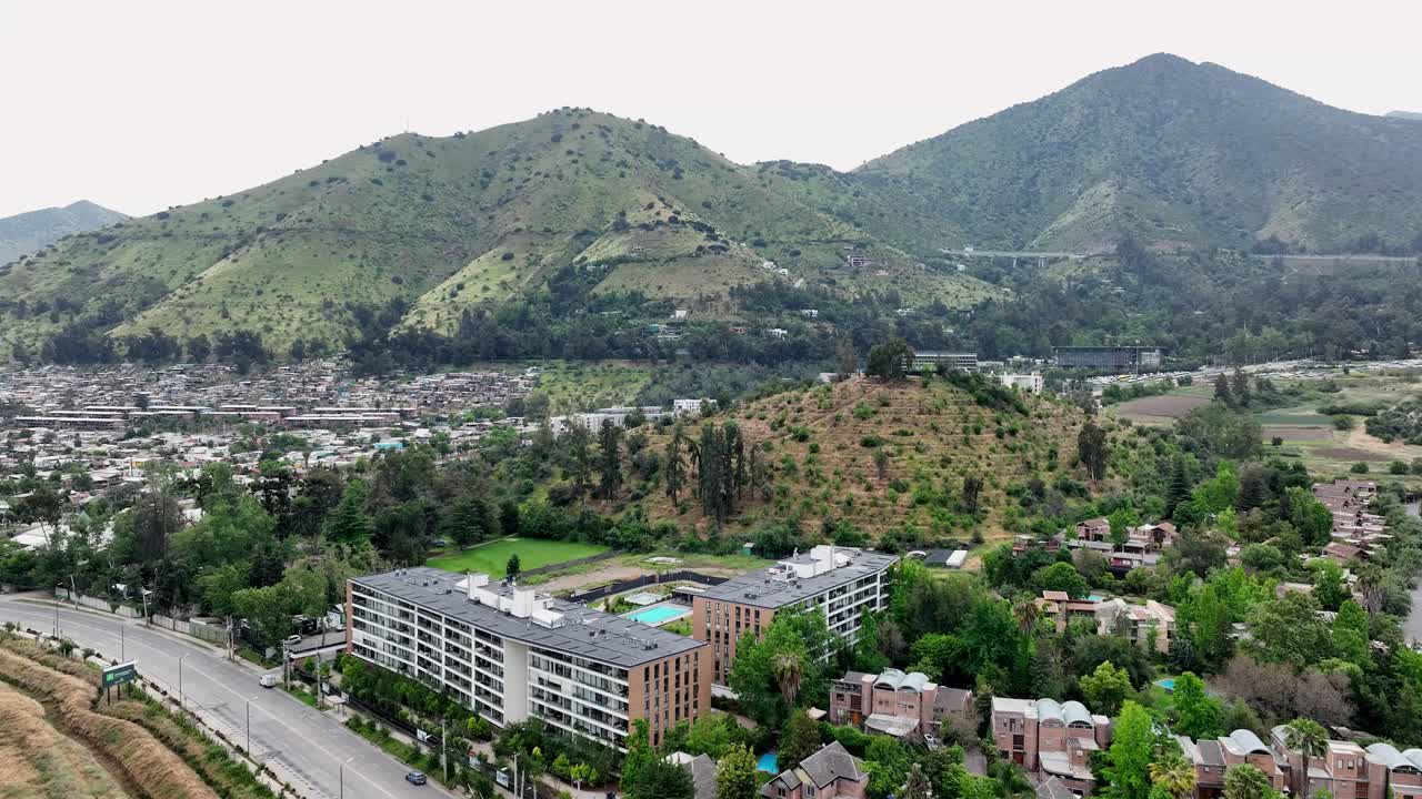 Panning drone aerial of modern residential apartments with pool, mountains backdrop, valley cityscape, and green neighborhood landscape