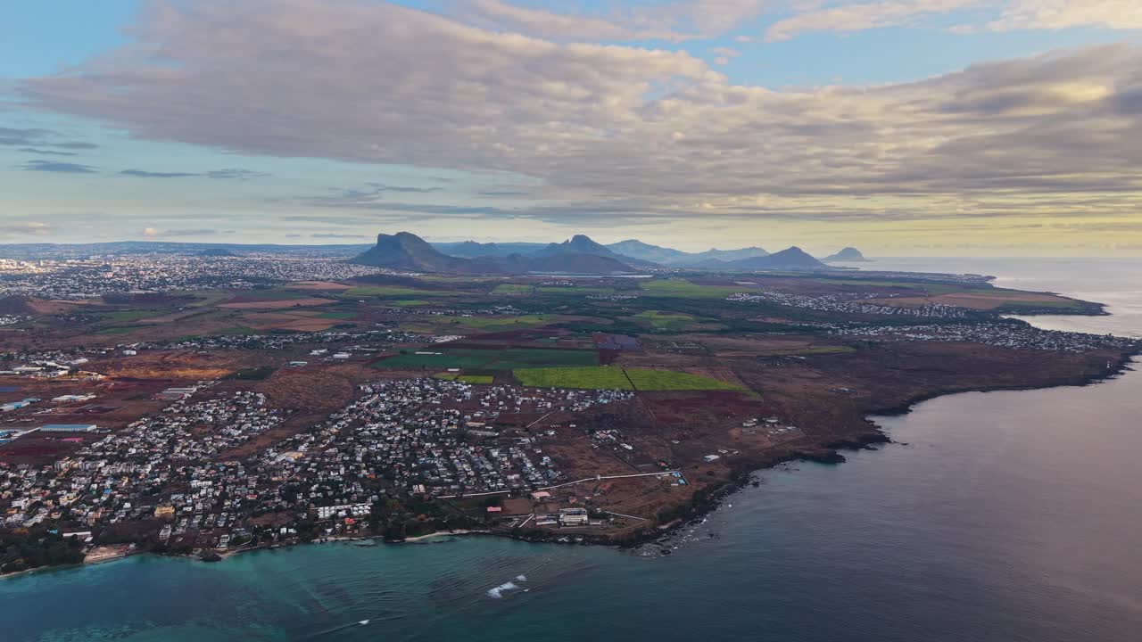 Wide aerial shot of Mauritius at sunset, revealing the island’s coastline, cityscape, and volcanic mountains bathed in golden light