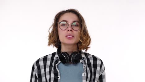 mujer joven atractiva con auriculares en el cuello soplando burbuja de chicle con los ojos abiertos aislados sobre fondo blanco. chicle estalla en la barbilla y ella está empezando a reír. cámara lenta