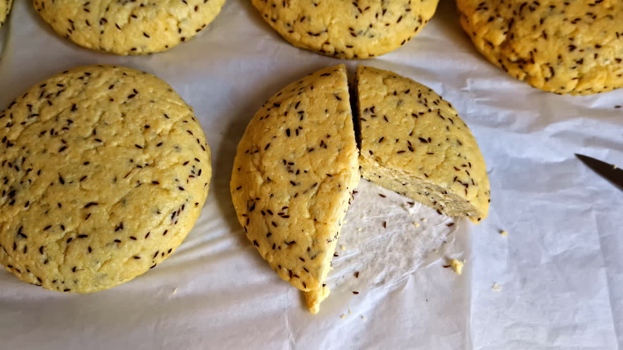 Freshly prepared solstice cheese with cumin seeds, one round sliced open on parchment paper