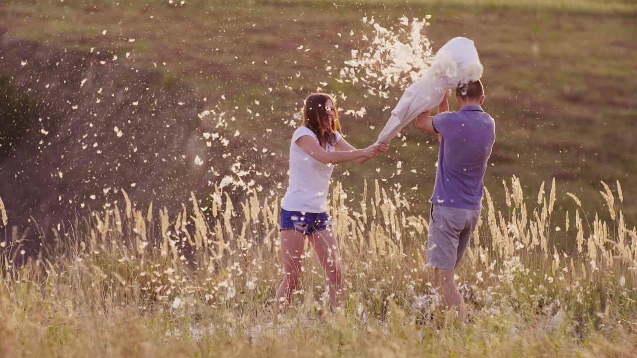 젊은 사람들은 미친 듯이 즐겁게 지내고 있다 한 여자는 친구와 함께 베개를 때리고 있다 깃털이 날고 있다