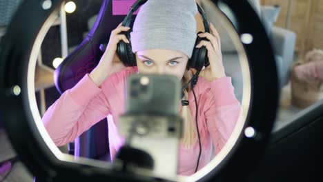 young female teenager puts her phone on the ring light while getting ready for streaming