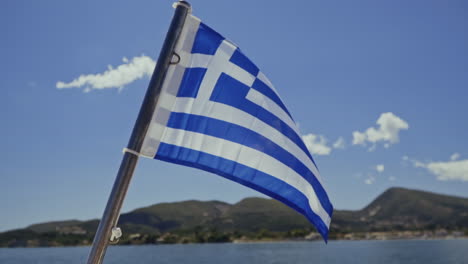 national flag of greece blows in the wind on boat with sea and coast behind