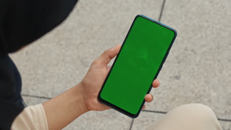 person holding a smartphone with a green screen