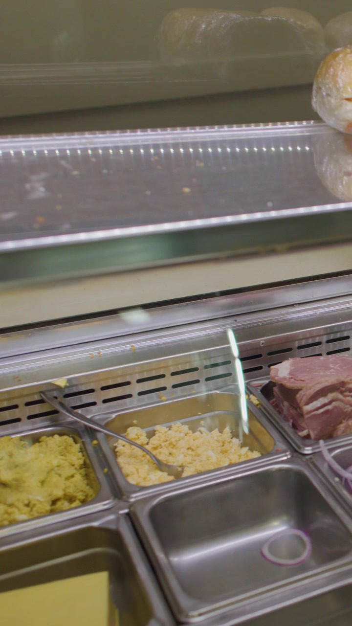 Salad bar di panetteria con farciture per panini, panini e salumi sotto una luminosa illuminazione interna.