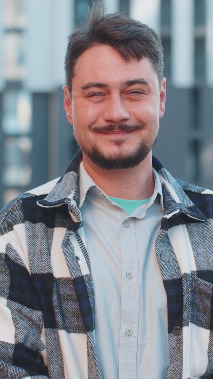 Happy mature man tourist using smartphone and looking at camera while standing in downtown street