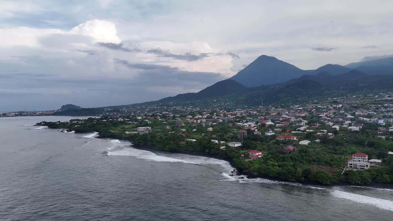 Uma perspectiva aérea de drone em um ângulo alto da cidade costeira de Limbe, Camarões, com o majestoso Monte Camarões se elevando no plano de fundo enevoado