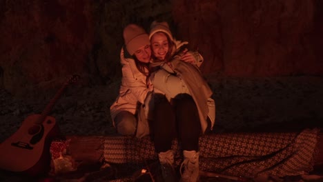two friends cuddling by a campfire