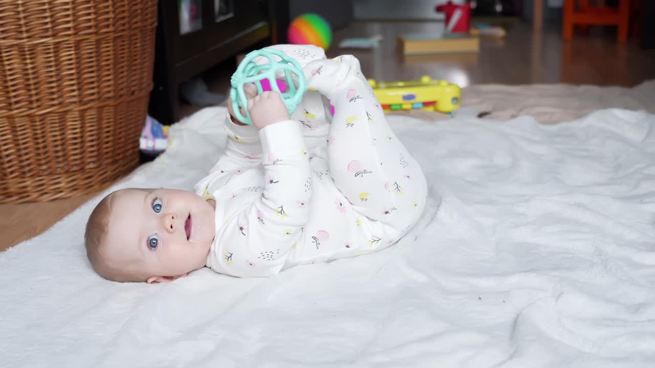 Baby girl plays with stacking toy rings while lying on soft bed at home setting