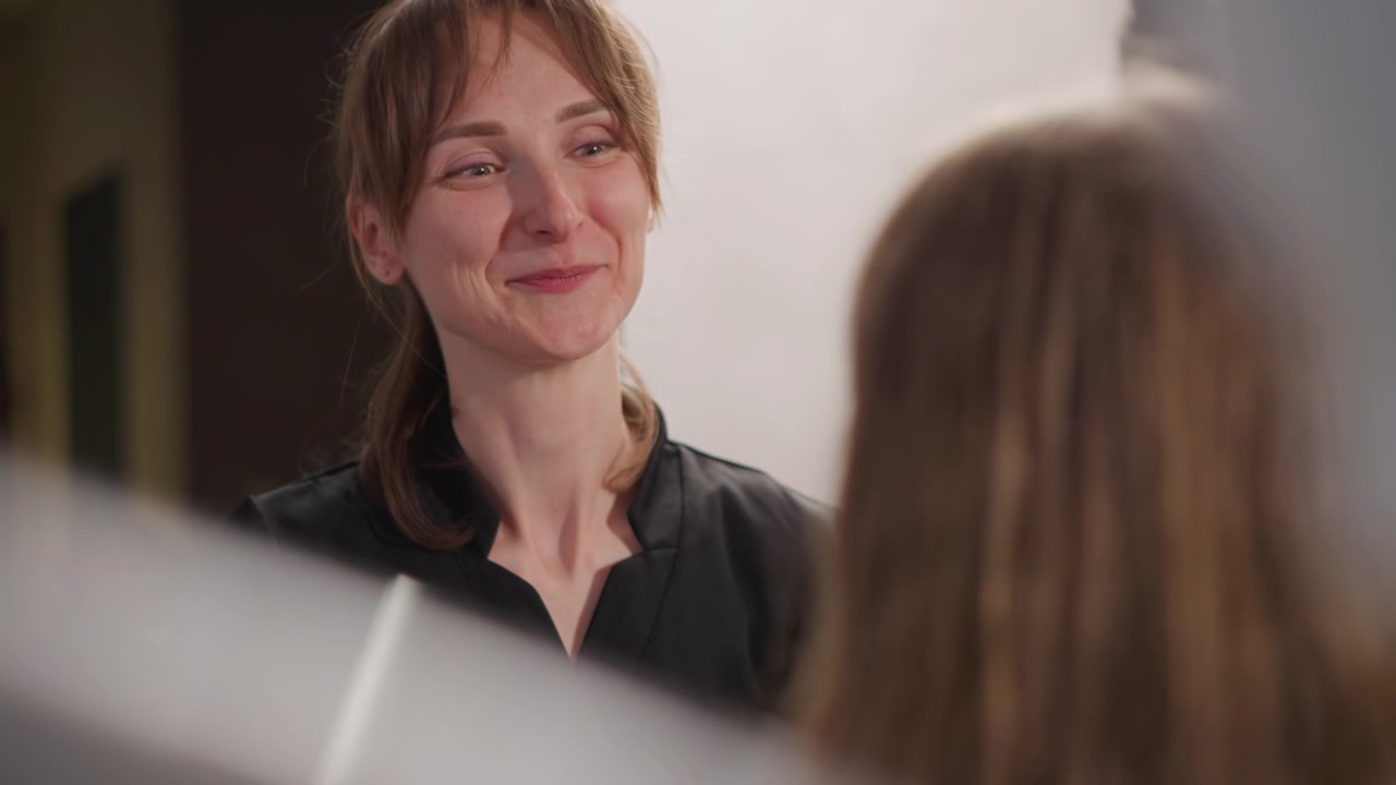 Primo piano di una donna che consulta un'altra donna in una consulenza ortodontica, spiegando le opzioni di trattamento. La professionista gesticola e parla alla paziente riguardo i dettagli della cura dentale. Luce soffusa