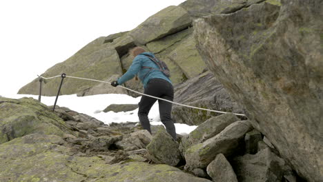 una mujer escalando terrenos empinados, rocosos y nevados usando una cuerda en un día nublado en noruega, cámara lenta