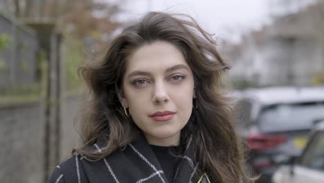 portrait of a gorgeous brunette woman smiling looking at camera standing in the middle of modern urban city street, wearing spring coat