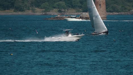 a speedboat quickly moves through ocean water in front of rocky shore and other boats as camera tracks