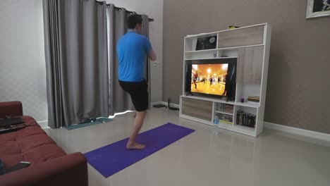 a man in his 30s is doing high knee oblique twists in front of a television in his living room following a fitness programme routine and trying to lose some weight