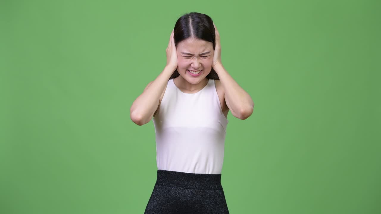 젊은 아름다운 아시아 사업가 여성이 큰 소음으로부터 귀를 고 있습니다.