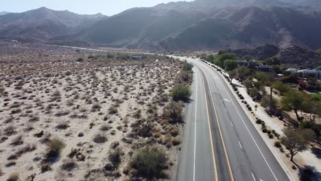 green vibrant town surrounded by hilly desert landscape and highway road, aerial drone shot