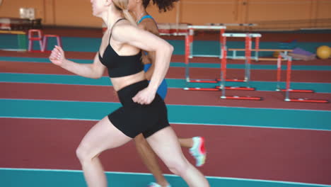 side view of two multiethnic female athletes running together on an indoor track 2