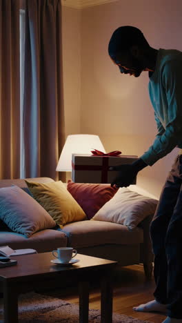 man holding a christmas gift in a living room at night