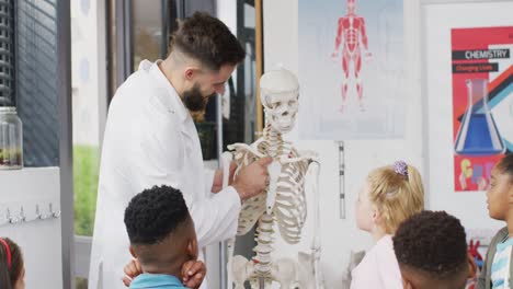 un maestro masculino diverso y escolares felices estudiando el esqueleto en la clase de biología