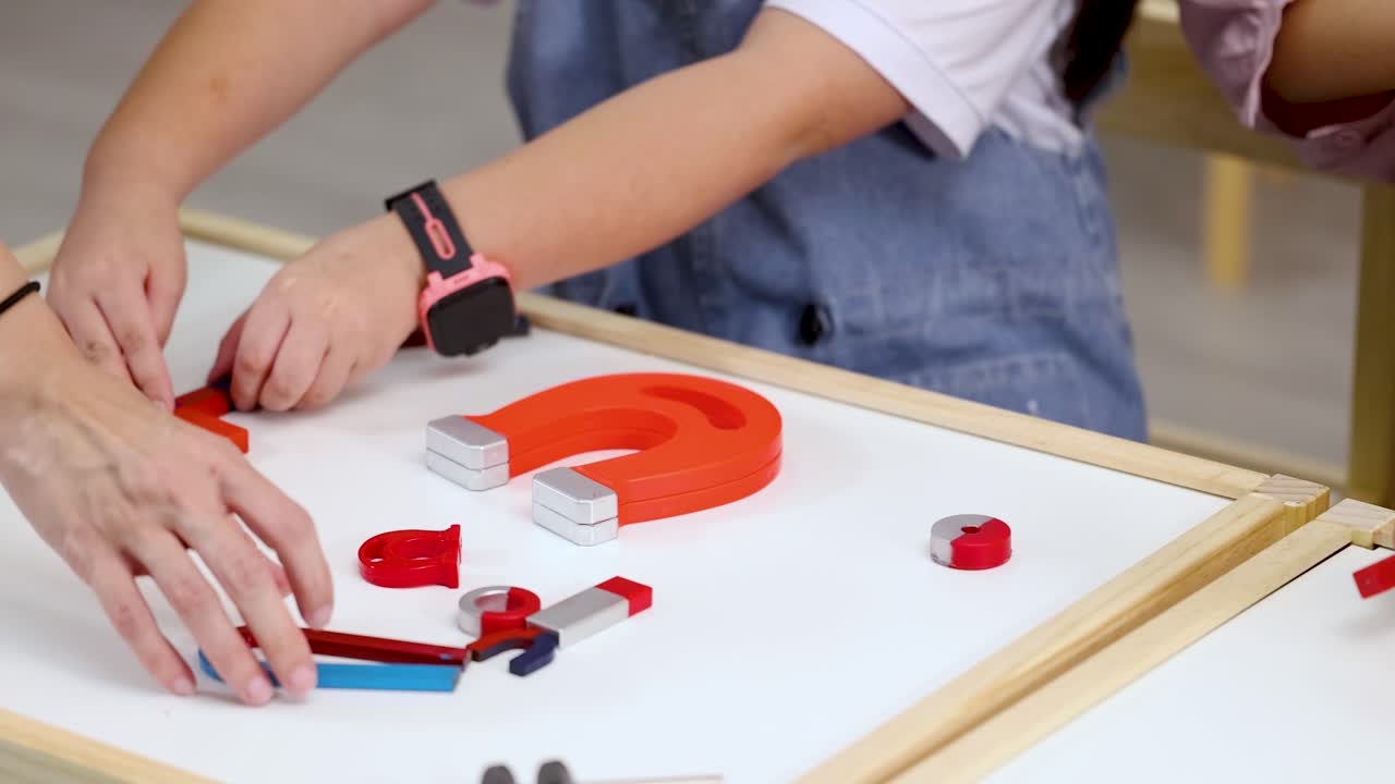 Close-up of students' hands manipulating various magnets on a white board during a physics experiment