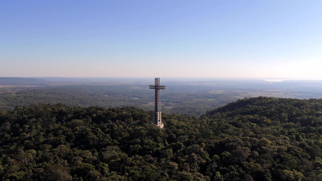 Um grande monumento em forma de cruz elevando-se acima de uma floresta densa em Santa Ana, Argentina, sob um céu azul claro. Ideal para documentários de viagem ou reportagens culturais.