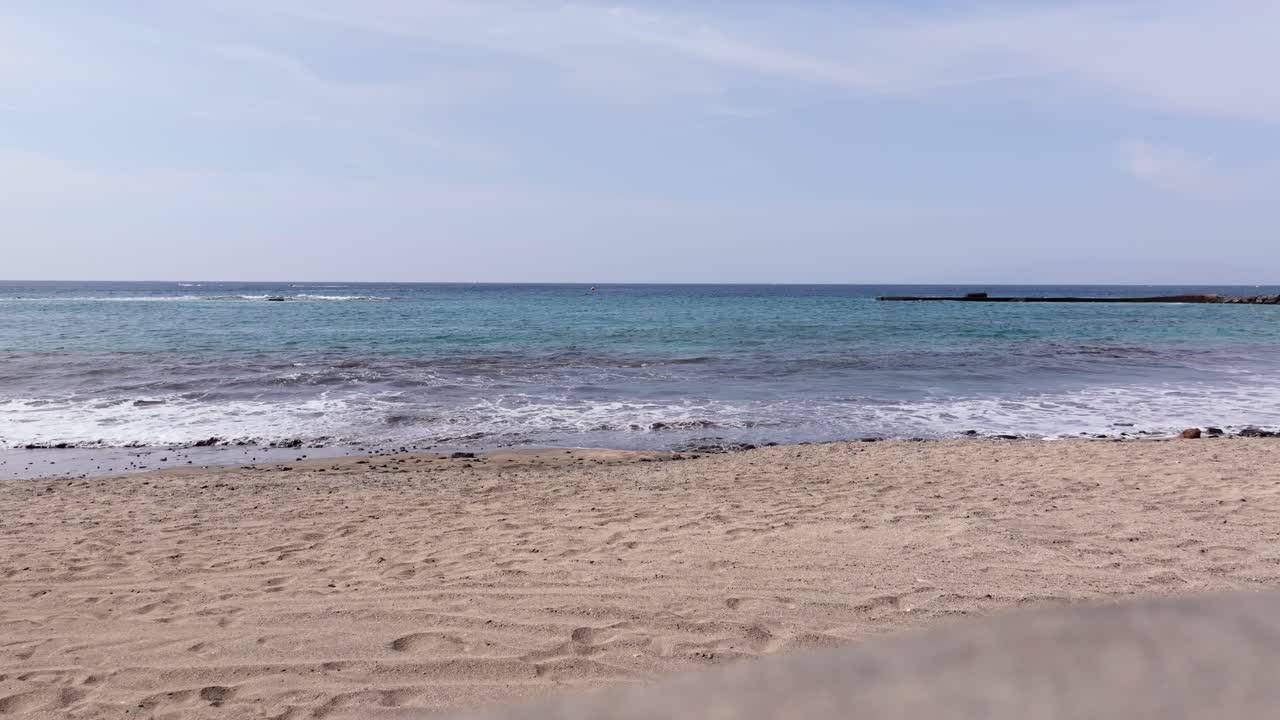 Soft waves wash ashore under a calm blue sky in Tenerife’s Costa Adeje beach