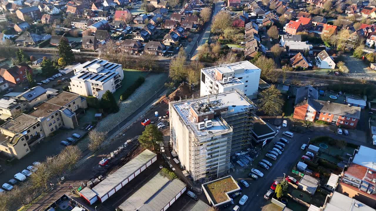 Construction site on high-rise apartment tower during sunset time in german town. Neighborhood With parking cars in winter. Aerial top down flyover.