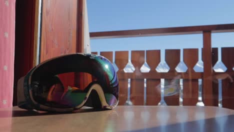 Dolly-in-slider-shot-of-a-ski-mask-on-a-wooden-table-during-daytime-with-bright-blue-sky