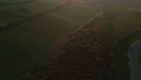 Aerial-view-of-a-landscape-during-sunset,-featuring-fields,-trees,-and-a-road